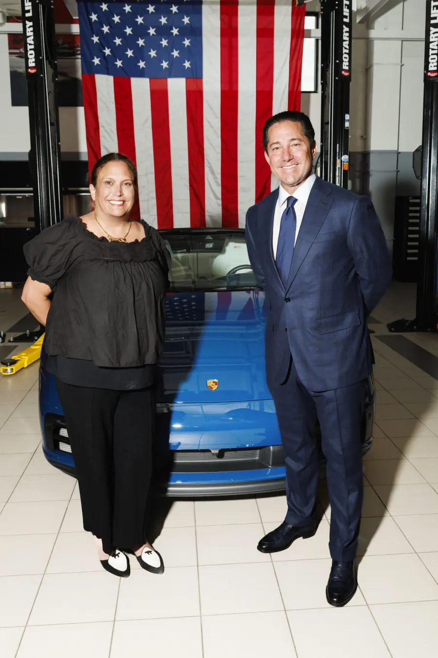 Todd Blue and Sarah standing in front of a blue Porsche in a dealership service area